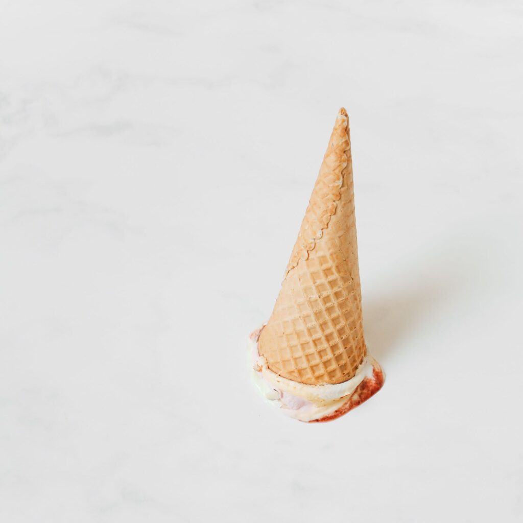 Ice cream cone that has fallen on the floor with the ice cream side down.