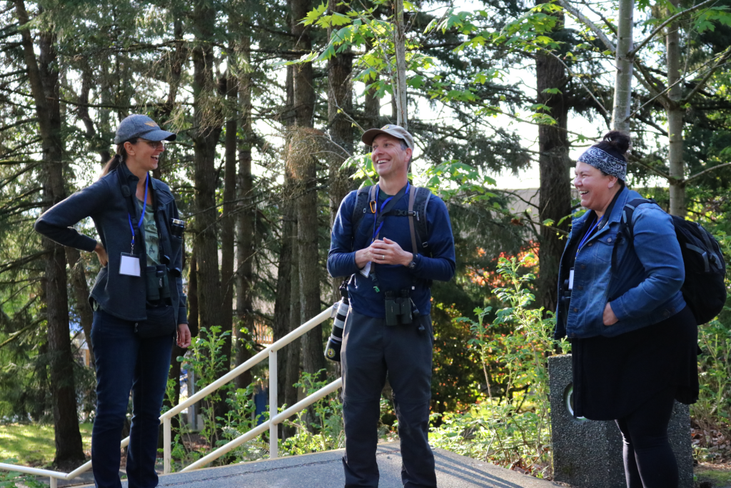 Three people standing outside at the VIU Nanaimo campus laughing in a semi-circle. 