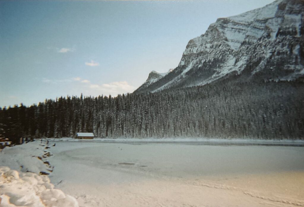 view on the frozen Lake Louise; the lake, the forest and mountains behind and a small cabin